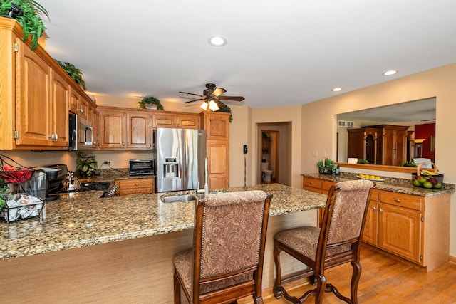 kitchen featuring kitchen peninsula, stainless steel appliances, a breakfast bar area, and light wood-type flooring