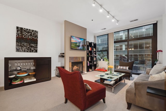 living room featuring carpet floors, a wall of windows, a tiled fireplace, and track lighting