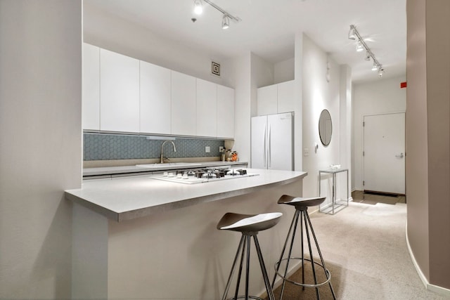 kitchen with white appliances, a kitchen bar, white cabinetry, light carpet, and backsplash