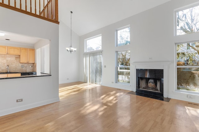 unfurnished living room with a tile fireplace, a towering ceiling, sink, and light wood-type flooring