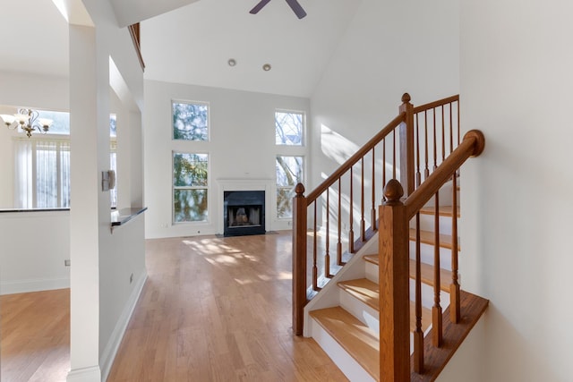 interior space with a healthy amount of sunlight, ceiling fan with notable chandelier, high vaulted ceiling, and light wood-type flooring