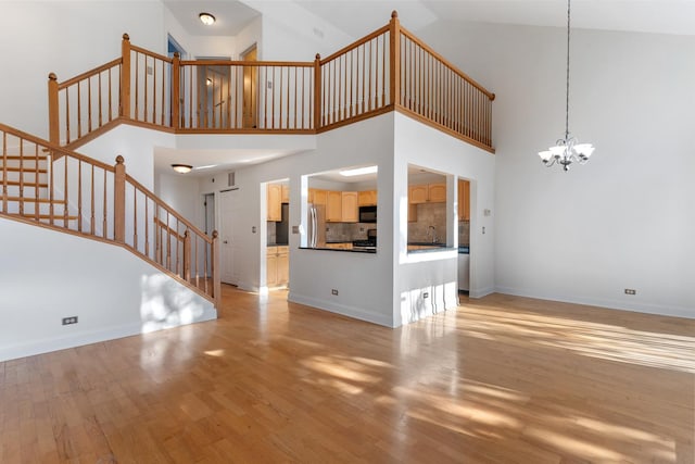 unfurnished living room with an inviting chandelier, sink, light hardwood / wood-style flooring, and a high ceiling