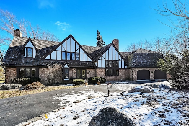 tudor-style house with a garage, driveway, brick siding, and a chimney