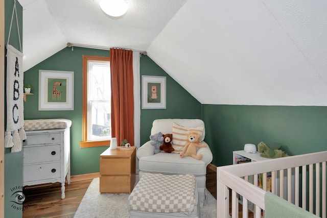 bedroom with vaulted ceiling, a nursery area, a textured ceiling, and hardwood / wood-style floors