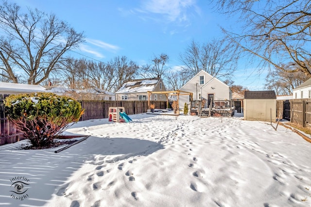 yard covered in snow with a storage shed, a deck, and a playground