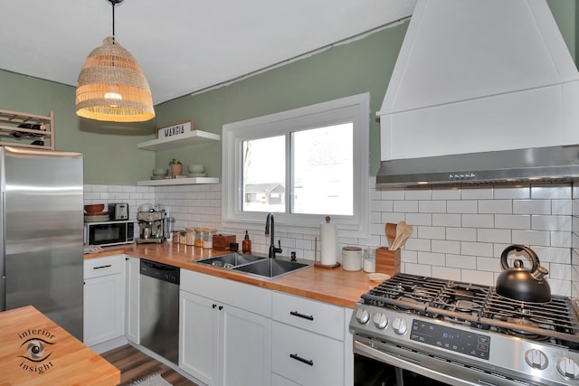 kitchen with decorative light fixtures, wood counters, stainless steel appliances, and custom range hood