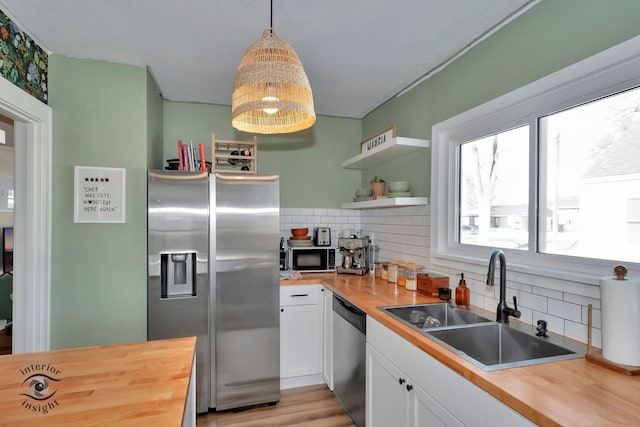 kitchen featuring pendant lighting, white cabinets, appliances with stainless steel finishes, butcher block counters, and sink