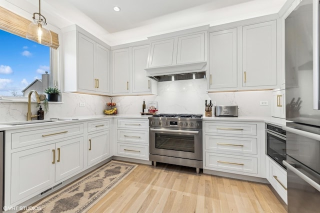 kitchen with appliances with stainless steel finishes, custom exhaust hood, decorative light fixtures, sink, and light wood-type flooring