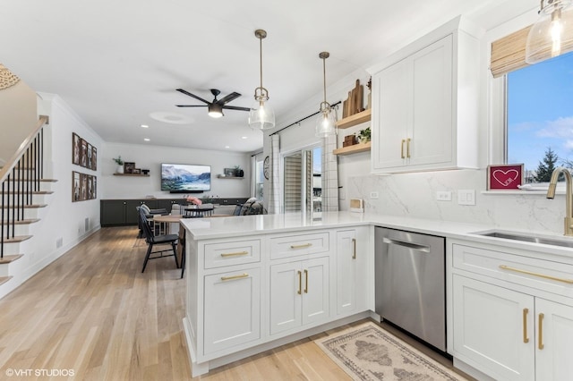 kitchen with kitchen peninsula, stainless steel dishwasher, sink, white cabinets, and decorative backsplash