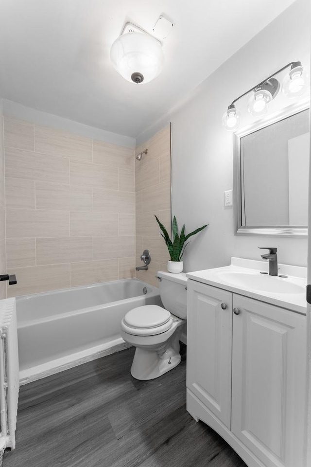 full bathroom with hardwood / wood-style floors, radiator, tiled shower / bath, vanity, and toilet