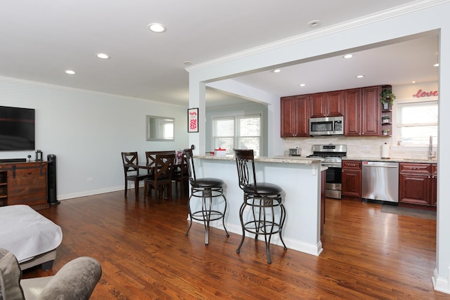 kitchen with a breakfast bar, dark hardwood / wood-style floors, backsplash, light stone counters, and stainless steel appliances