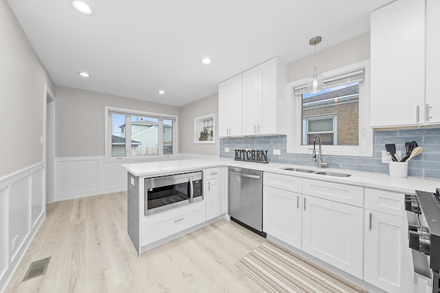 kitchen with pendant lighting, kitchen peninsula, sink, stainless steel appliances, and white cabinets