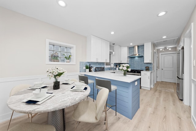 kitchen featuring white cabinetry, kitchen peninsula, a breakfast bar area, wall chimney exhaust hood, and sink