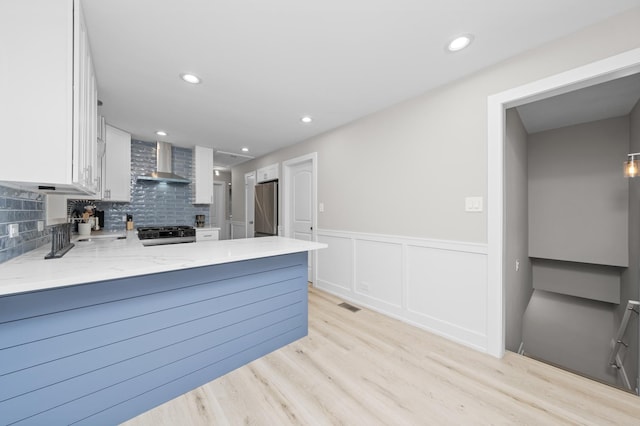 kitchen with decorative backsplash, white cabinetry, light stone countertops, stainless steel appliances, and wall chimney exhaust hood