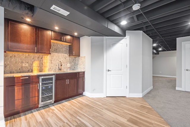 bar with wine cooler, sink, tasteful backsplash, light stone counters, and light wood-type flooring