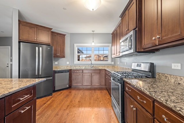 kitchen with sink, decorative light fixtures, light wood-type flooring, appliances with stainless steel finishes, and light stone countertops