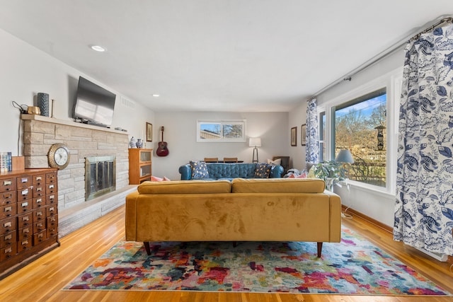 living room with a stone fireplace and light wood-type flooring