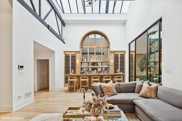 living room featuring a towering ceiling, indoor bar, and light hardwood / wood-style flooring