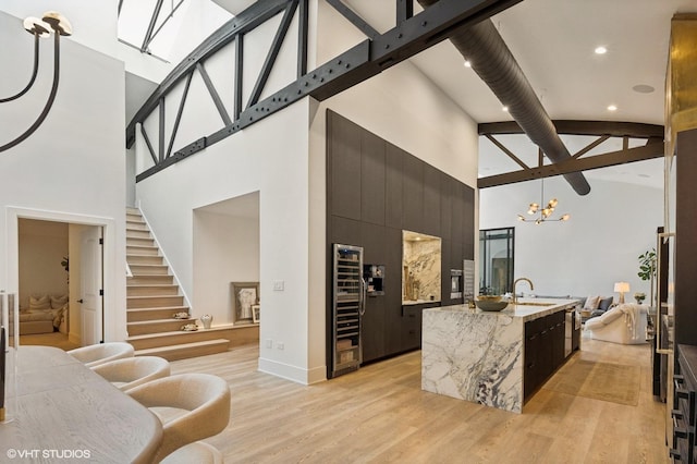 kitchen featuring a towering ceiling, light hardwood / wood-style flooring, decorative light fixtures, and an island with sink