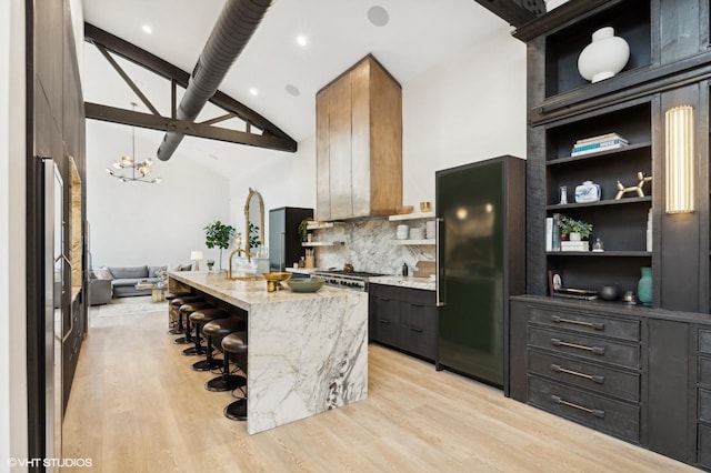 kitchen featuring backsplash, a kitchen breakfast bar, built in refrigerator, a kitchen island with sink, and light stone counters