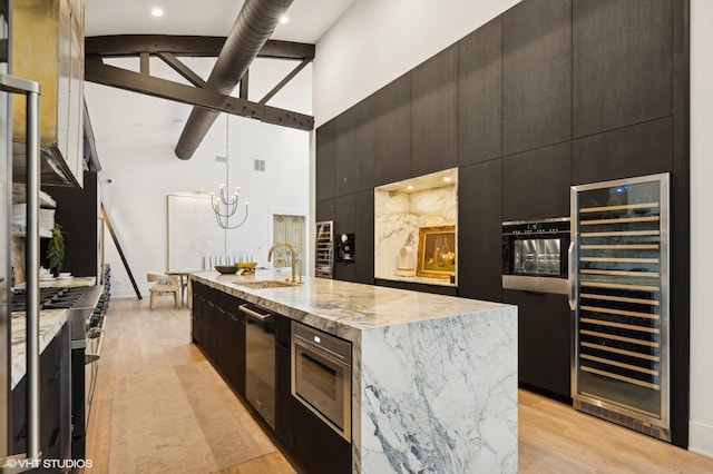 kitchen with sink, a kitchen island with sink, a towering ceiling, beverage cooler, and light hardwood / wood-style floors