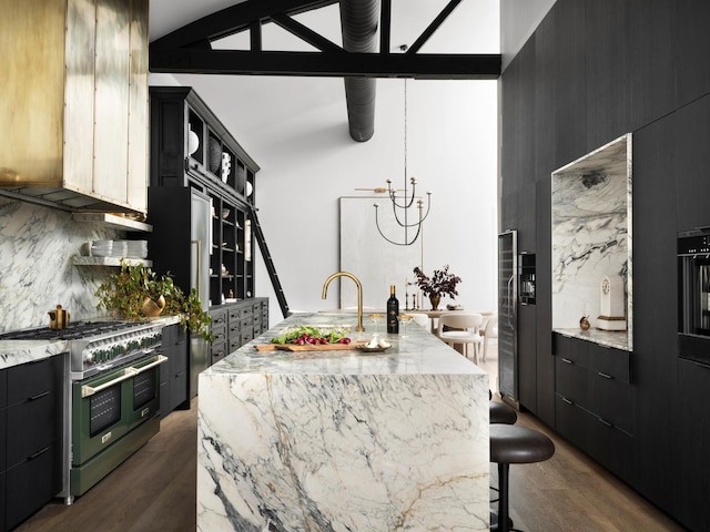 kitchen featuring dark wood-type flooring, double oven range, light stone countertops, a center island with sink, and decorative backsplash