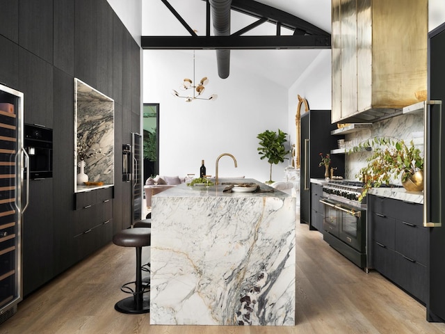 kitchen featuring vaulted ceiling, a breakfast bar area, range with two ovens, light hardwood / wood-style floors, and a center island with sink