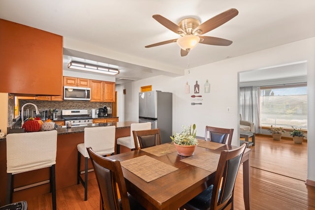 dining space with ceiling fan, beamed ceiling, and light hardwood / wood-style flooring