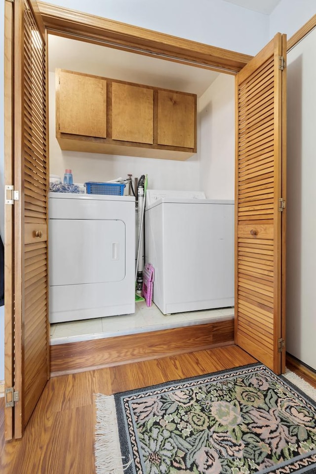 clothes washing area with cabinets, washer and dryer, and light hardwood / wood-style flooring