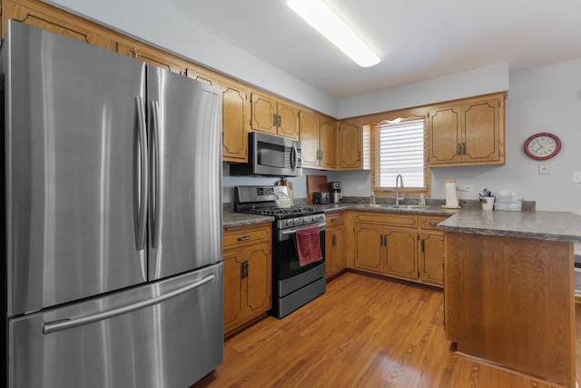 kitchen featuring appliances with stainless steel finishes, kitchen peninsula, sink, and light wood-type flooring