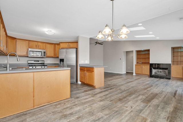 kitchen featuring ceiling fan with notable chandelier, vaulted ceiling with skylight, stainless steel appliances, sink, and light hardwood / wood-style flooring