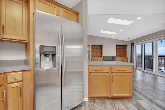 kitchen featuring lofted ceiling with skylight, stainless steel fridge with ice dispenser, light brown cabinets, and light hardwood / wood-style floors