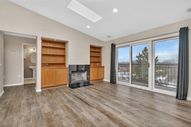 unfurnished living room featuring a fireplace, built in shelves, lofted ceiling with skylight, and dark wood-type flooring