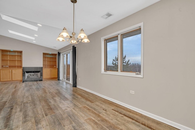 unfurnished living room featuring lofted ceiling, a notable chandelier, a fireplace, wood-type flooring, and built in features