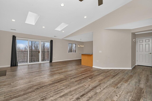 unfurnished living room with a skylight, ceiling fan with notable chandelier, hardwood / wood-style flooring, and high vaulted ceiling