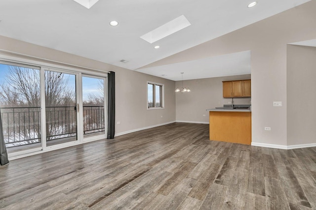 unfurnished living room featuring dark wood-type flooring, lofted ceiling with skylight, and a chandelier