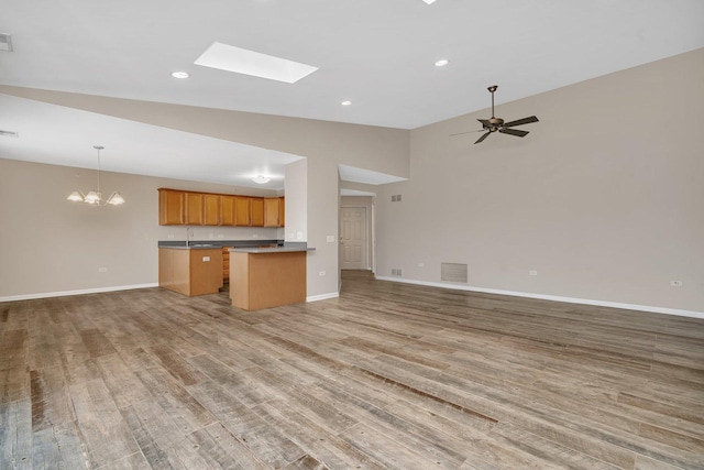 kitchen with ceiling fan with notable chandelier, vaulted ceiling with skylight, decorative light fixtures, kitchen peninsula, and light wood-type flooring