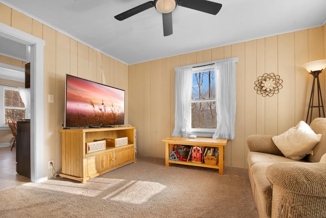 sitting room with ceiling fan, light colored carpet, and wooden walls