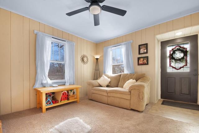 living room with wood walls, ceiling fan, and carpet floors