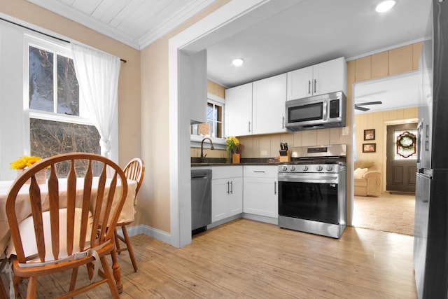 kitchen with white cabinets, stainless steel appliances, sink, ornamental molding, and light wood-type flooring