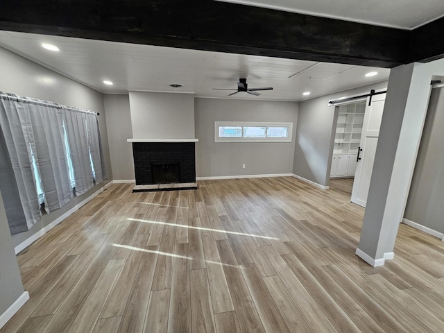 unfurnished living room featuring a brick fireplace, ceiling fan, a barn door, and light wood-type flooring