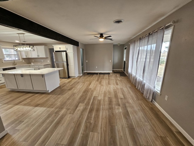 kitchen featuring light hardwood / wood-style floors, stainless steel fridge, hanging light fixtures, a kitchen island, and white cabinets