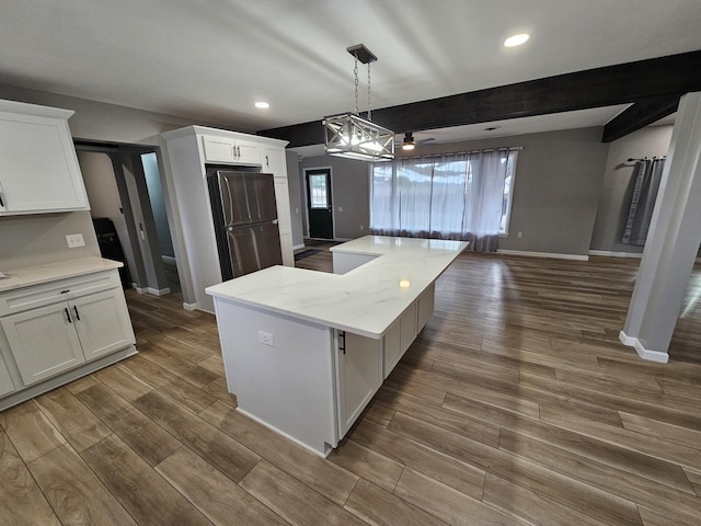 kitchen with white cabinetry, stainless steel fridge, pendant lighting, light stone counters, and a center island