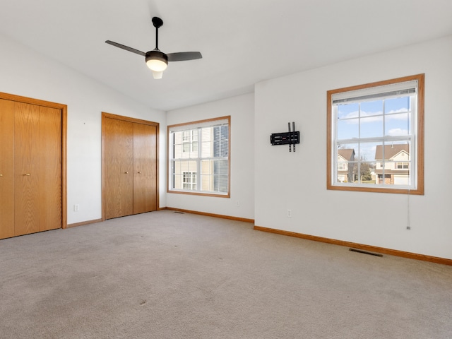 unfurnished bedroom with lofted ceiling, ceiling fan, two closets, and light colored carpet