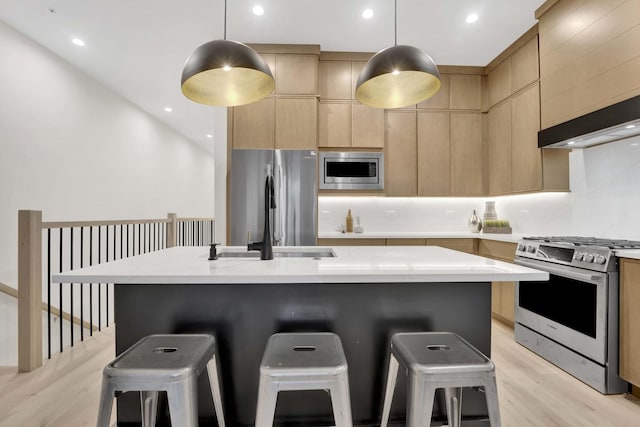 kitchen with light brown cabinetry, appliances with stainless steel finishes, a kitchen breakfast bar, modern cabinets, and a sink