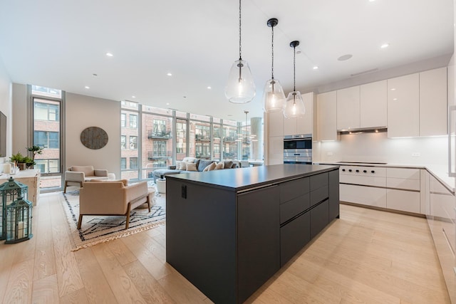 kitchen with white cabinets, a wall of windows, hanging light fixtures, a center island, and light hardwood / wood-style flooring