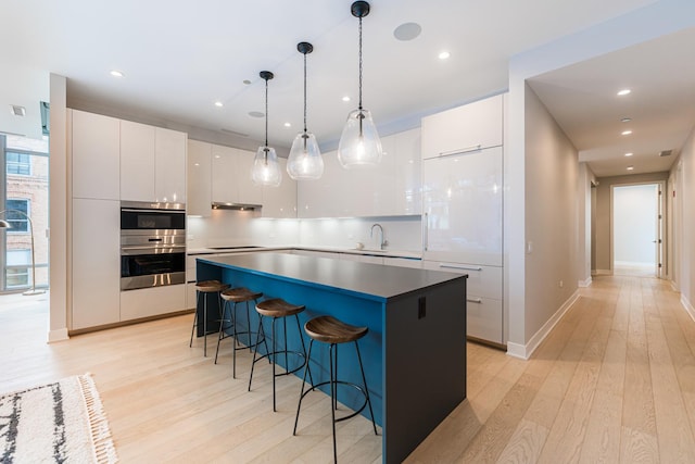 kitchen featuring sink, light hardwood / wood-style flooring, a kitchen island, pendant lighting, and white cabinets