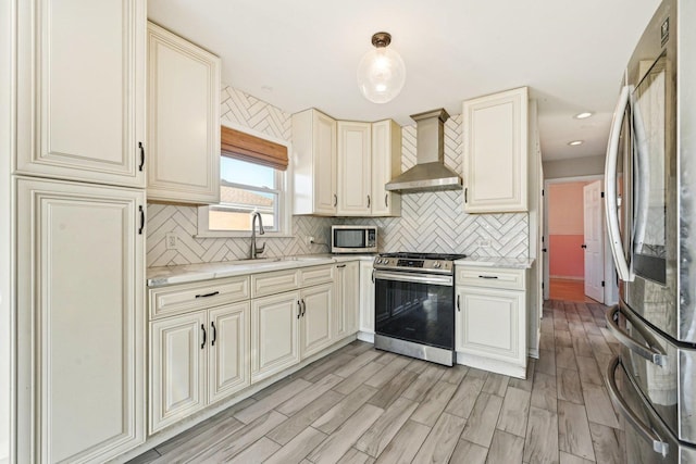 kitchen with wall chimney exhaust hood, sink, hanging light fixtures, appliances with stainless steel finishes, and cream cabinetry