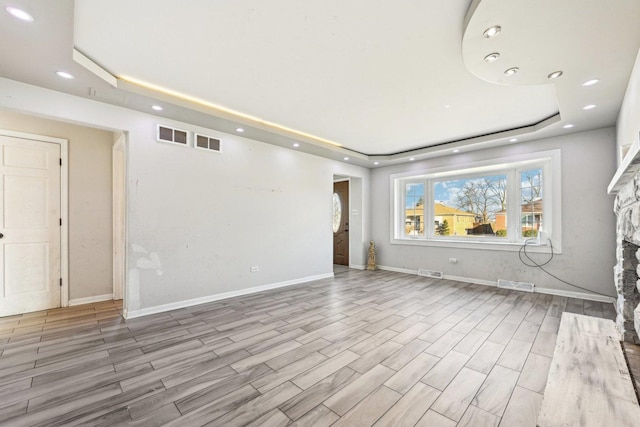 unfurnished living room featuring a stone fireplace, a raised ceiling, and light wood-type flooring