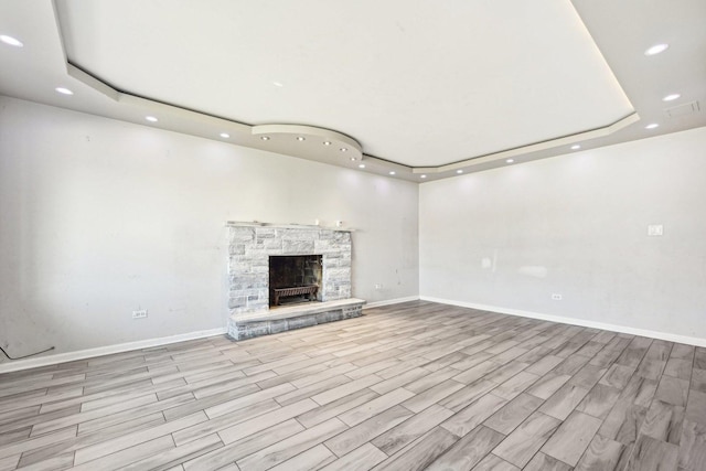 unfurnished living room featuring light hardwood / wood-style flooring, a fireplace, and a tray ceiling